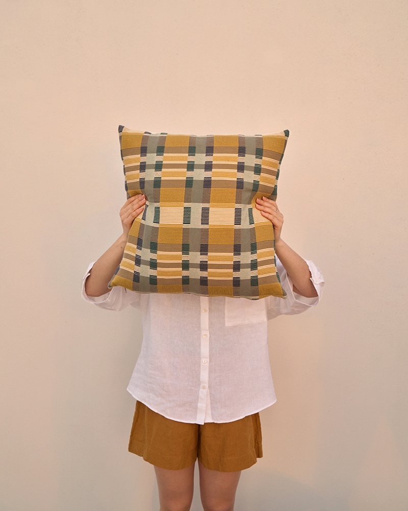 A model covering her face with a colourful checked Skipping Block Cushion Cover. Woven by Mungo in South Africa. 100% cotton cushion covers.