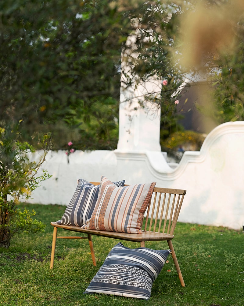The Mungo Sahara Stripe Cushion Covers on a bench in a garden. Homeware textiles woven in South Africa