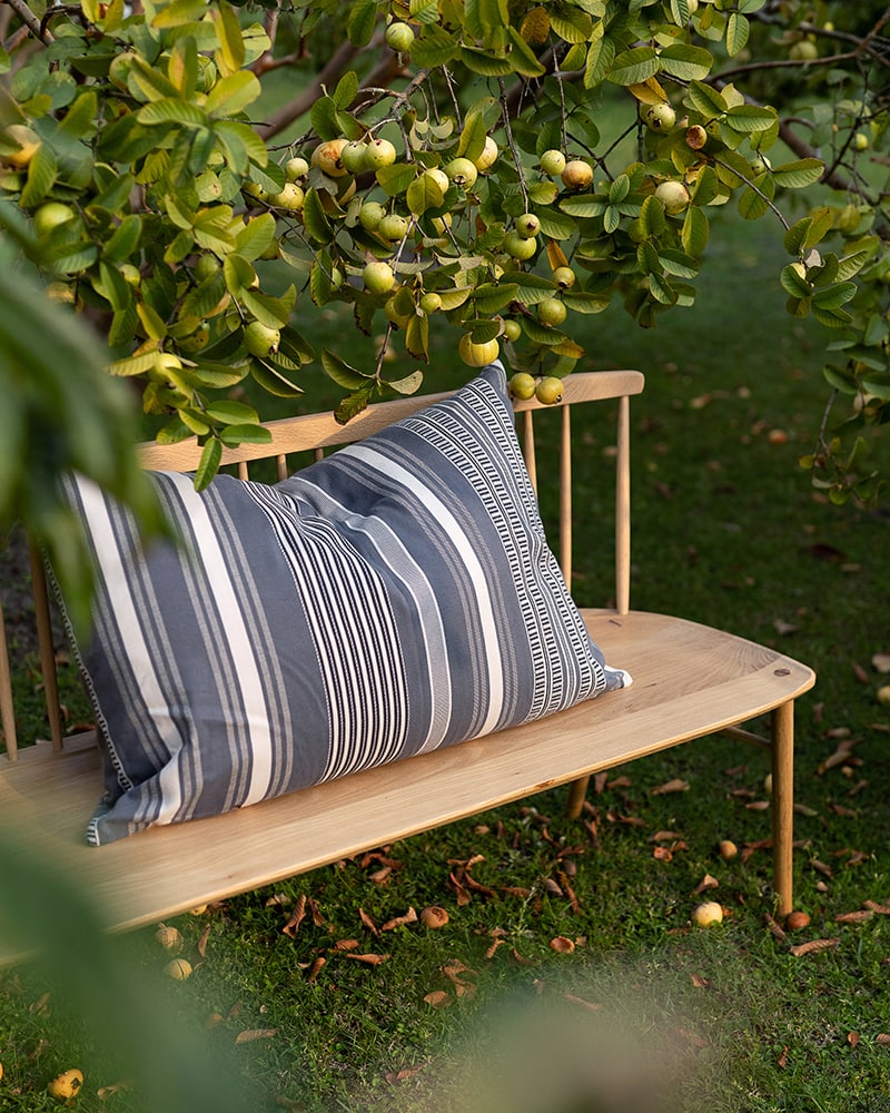 The Mungo Sahara Stripe Cushion Cover in Storm Cloud in an garden bench under a fruit tree