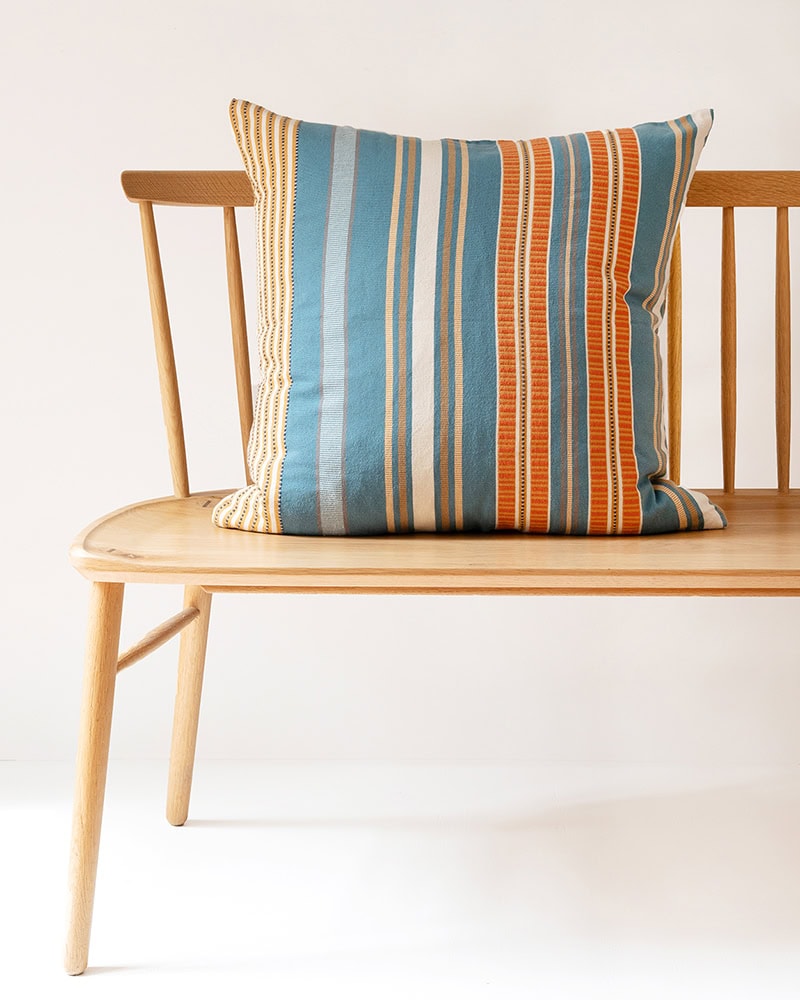 The Mungo Sahara Stripe Cushion Cover in Oasis colourway on a wooden bench