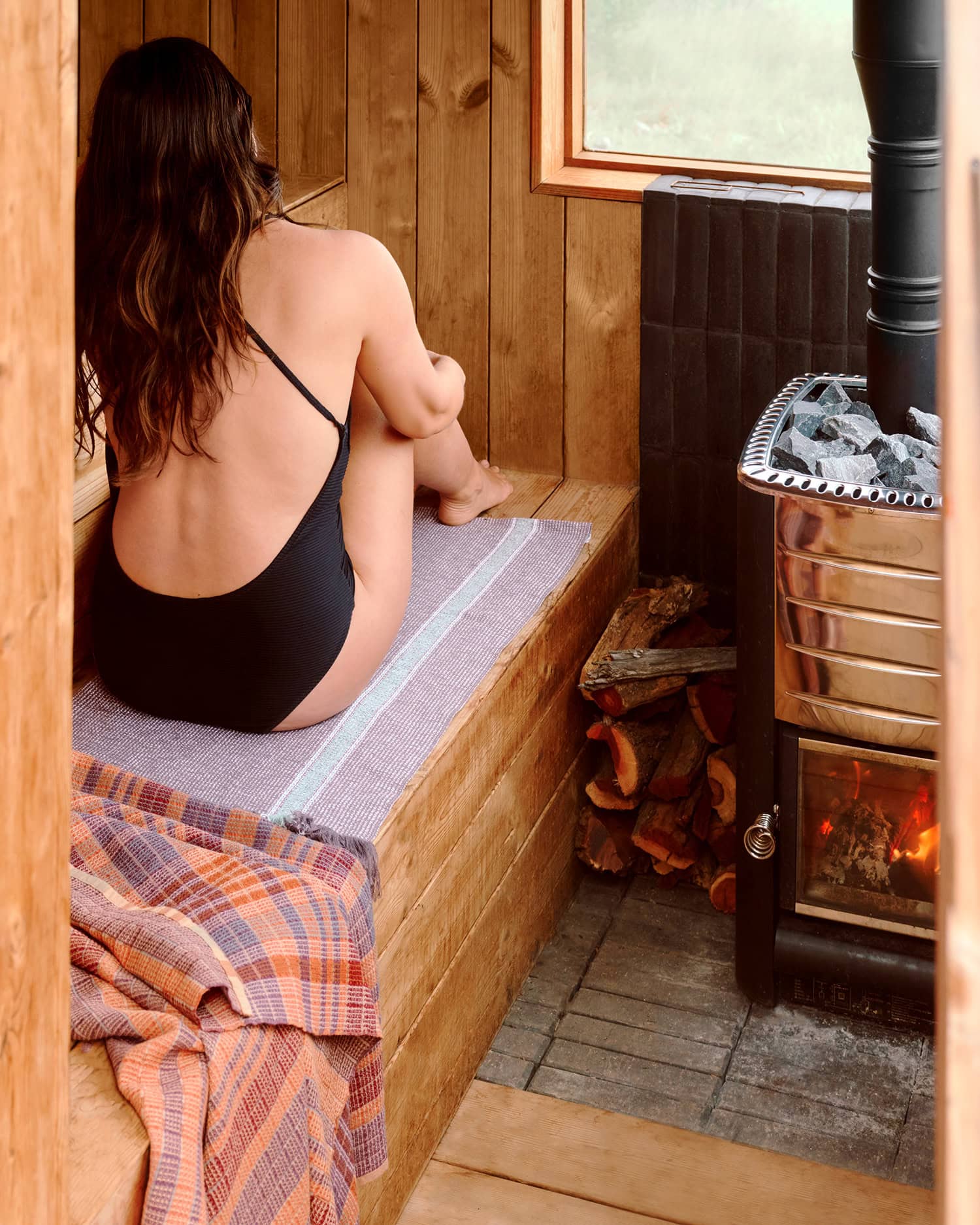 Model sitting in sauna on a Mungo Summer towel with a Wayfarer towel draped on the bench.