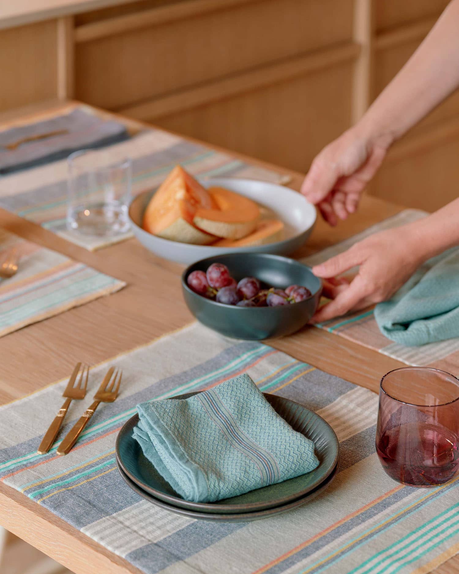 Model setting a table with Mungo placemats and napkins and fruit.